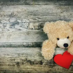 Miś pluszowy z czerwonym sercem na drewnianym tle.
